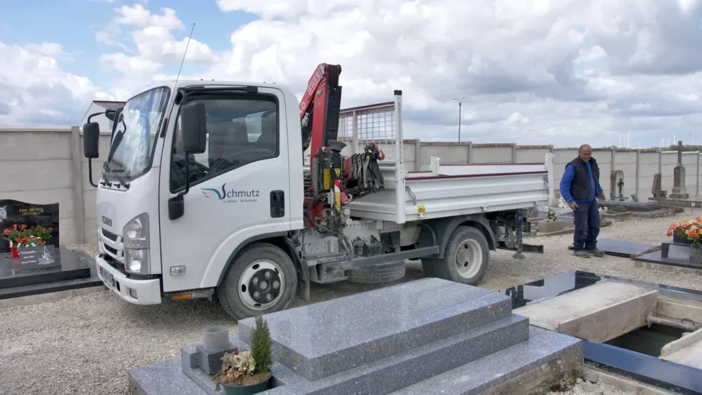 Camion de marbrerie des Pompes Funèbres Schmutz stationné dans un cimetière.